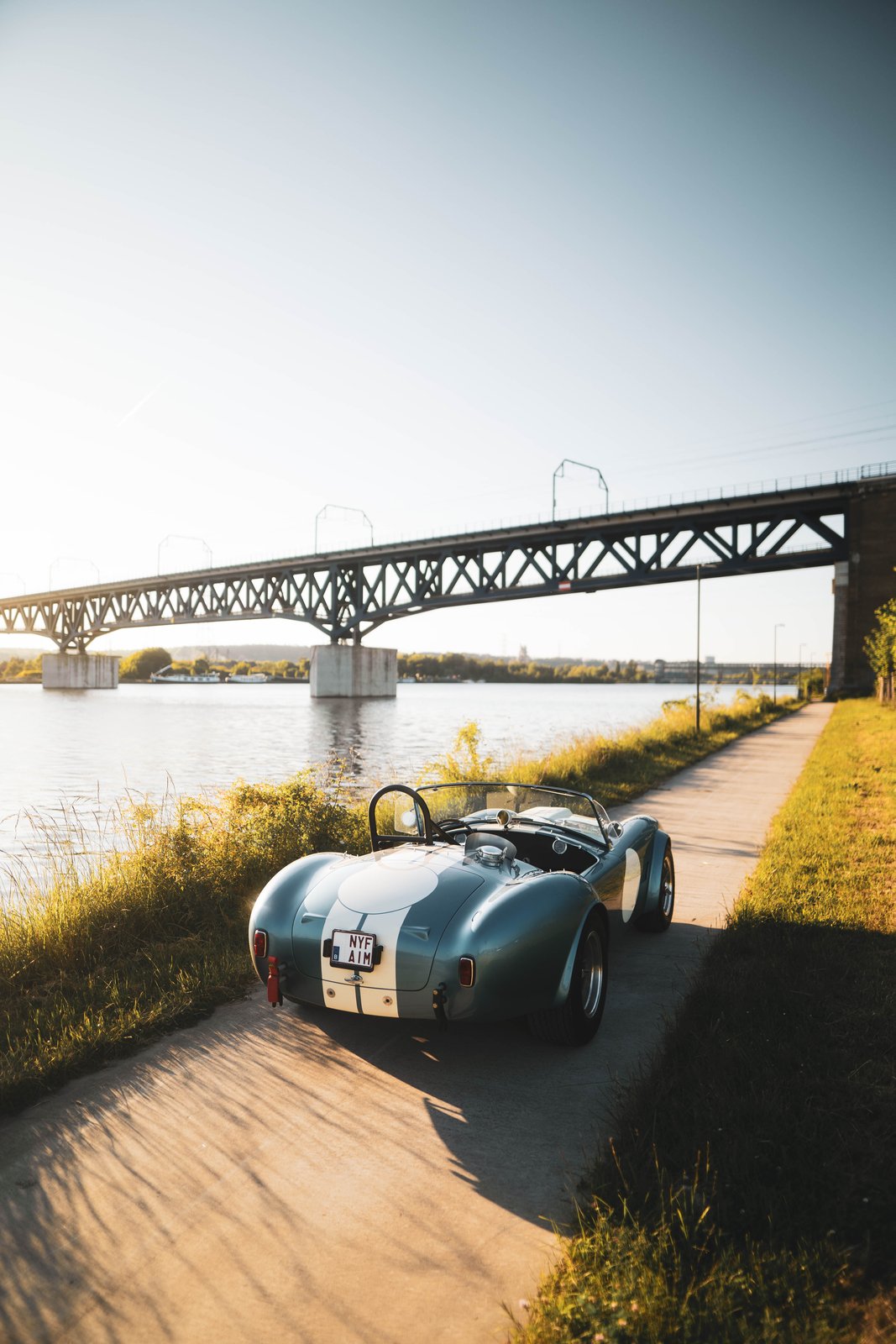 Shelby Cobra bleue de dos, devant un pont métallique