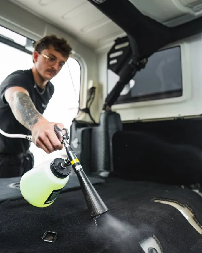 Killian, detailer à domicile près de Liège, applique un nettoyant moussant sur la moquette d'un véhicule